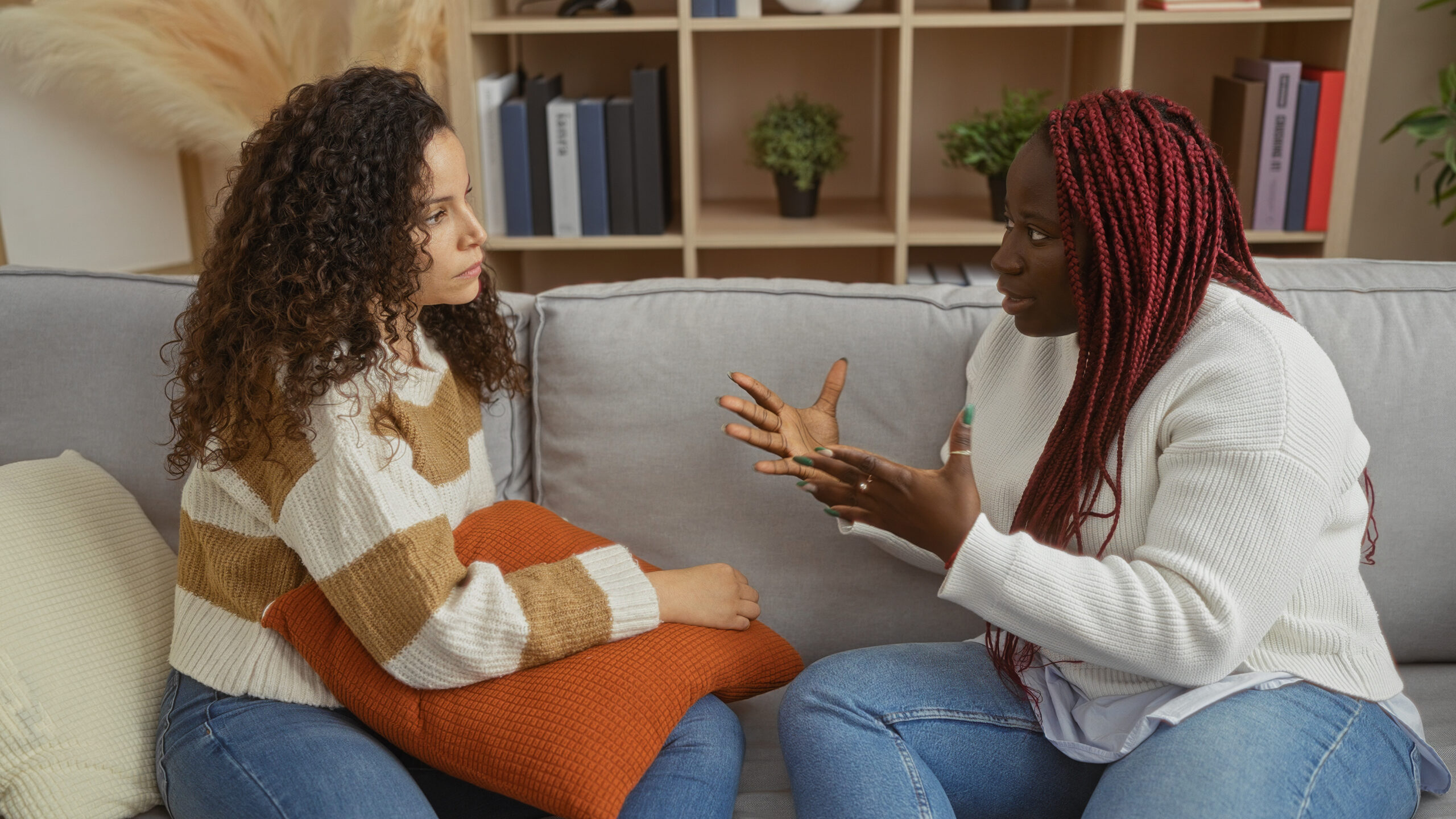 Two women friends sitting in a cozy living room engaged in a serious conversation